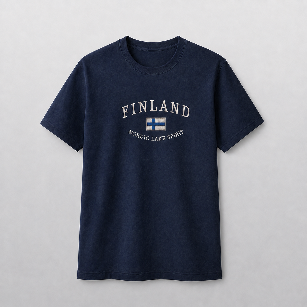 Tummansininen kirjailtu T-paita harmaalla studiotaustalla, FINLAND-teksti, Suomen lippu ja NORDIC LAKE SPIRIT